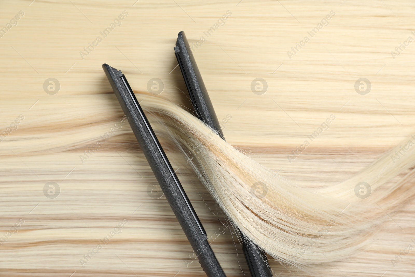 Photo of Modern flat iron on shiny blonde hair, top view