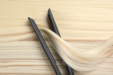 Photo of Modern flat iron on shiny blonde hair, top view