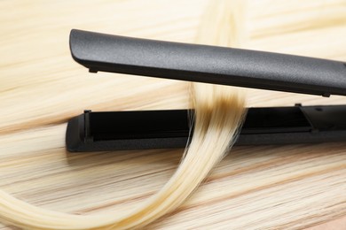 Photo of Modern flat iron on shiny blonde hair, closeup