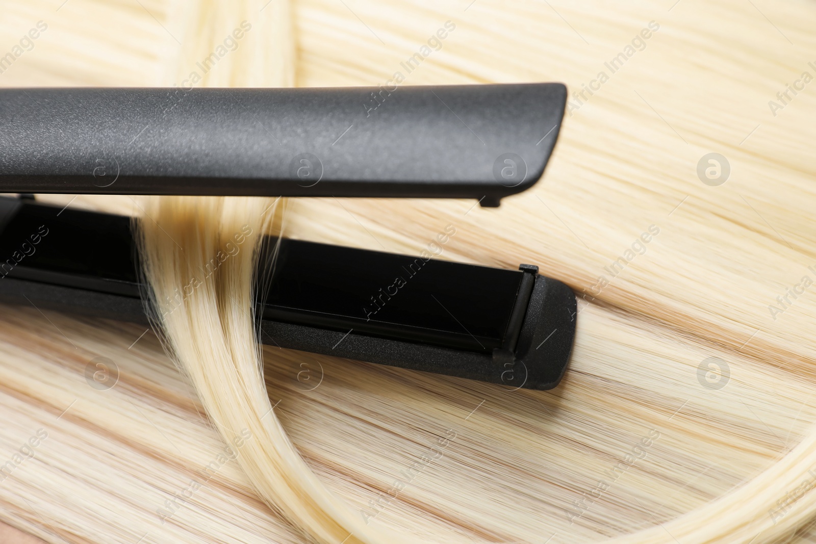 Modern flat iron on shiny blonde hair, closeup Photo of Modern flat iron on shiny blonde hair, closeup