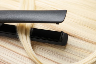 Photo of Modern flat iron on shiny blonde hair, closeup