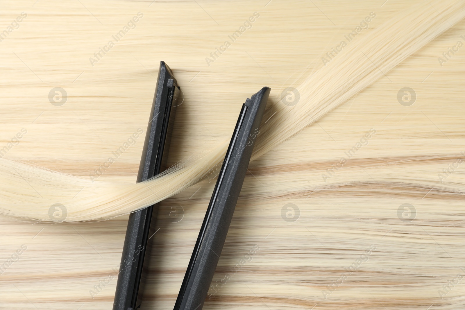 Modern flat iron on shiny blonde hair, top view Photo of Modern flat iron on shiny blonde hair, top view