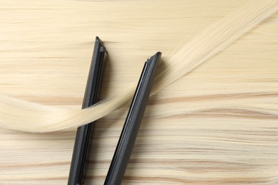 Photo of Modern flat iron on shiny blonde hair, top view