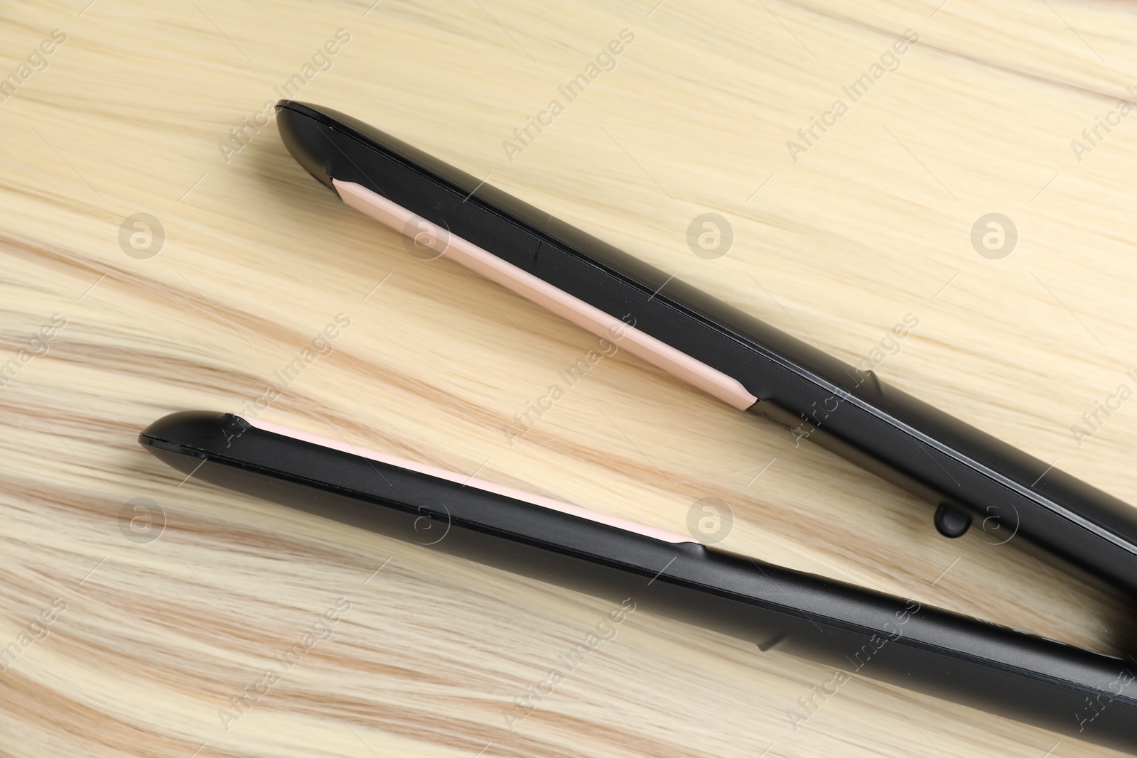 Photo of Modern flat iron on shiny blonde hair, top view