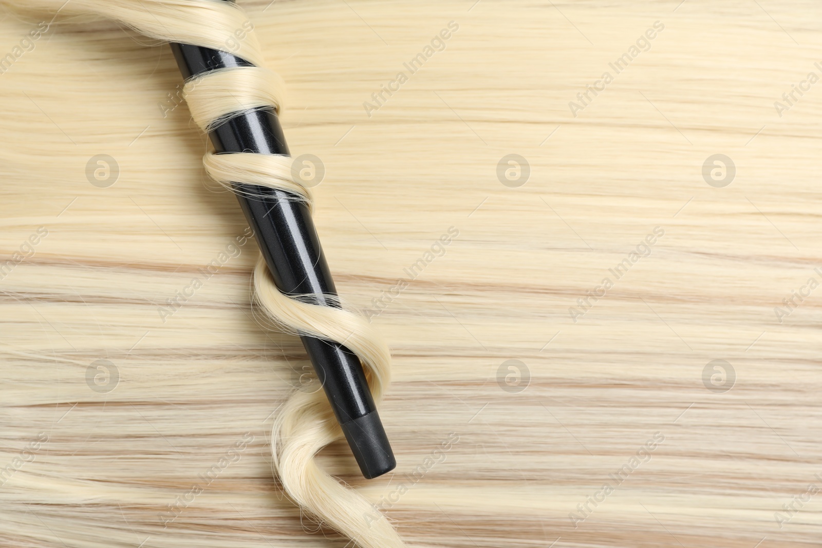 Curling iron with shiny blonde hair, top view Photo of Curling iron with shiny blonde hair, top view