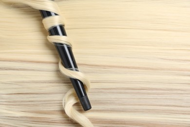 Photo of Curling iron with shiny blonde hair, top view