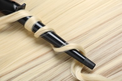 Photo of Curling iron with shiny blonde hair, closeup