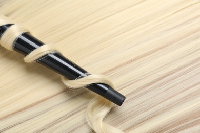Photo of Curling iron with shiny blonde hair, top view