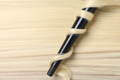 Photo of Curling iron with shiny blonde hair, top view