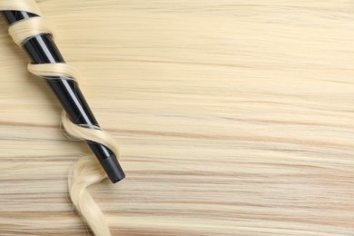 Photo of Curling iron with shiny blonde hair, top view