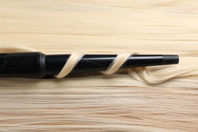Photo of Curling iron with shiny blonde hair, closeup
