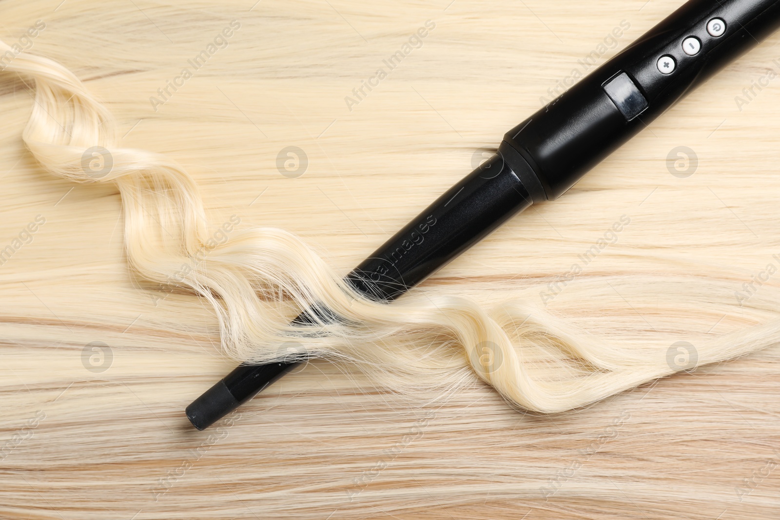 Photo of Curling iron with shiny blonde hair, top view
