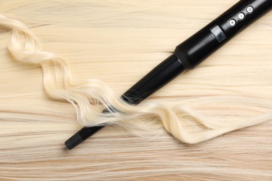 Photo of Curling iron with shiny blonde hair, top view