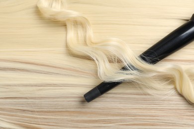 Photo of Curling iron with shiny blonde hair, top view