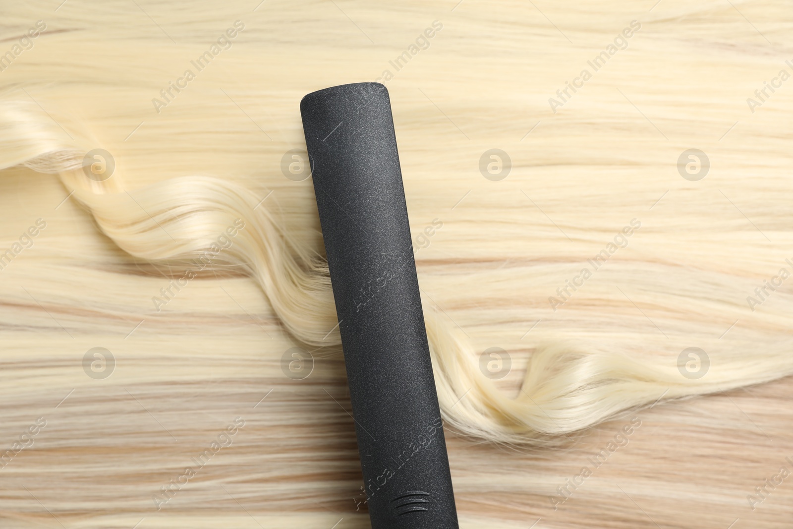 Modern flat iron on shiny blonde hair, top view Photo of Modern flat iron on shiny blonde hair, top view