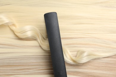Photo of Modern flat iron on shiny blonde hair, top view