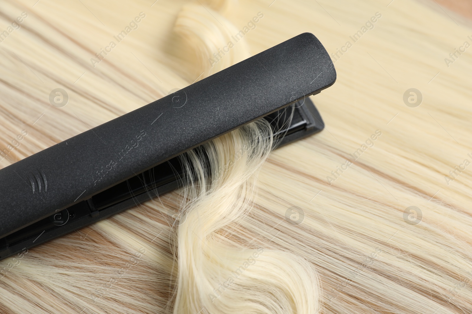 Modern flat iron on shiny blonde hair, closeup Photo of Modern flat iron on shiny blonde hair, closeup