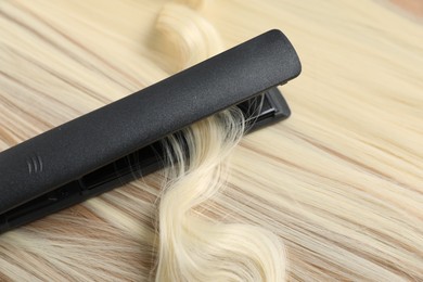 Photo of Modern flat iron on shiny blonde hair, closeup