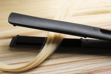 Photo of Modern flat iron on shiny blonde hair, closeup