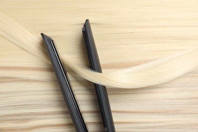 Photo of Modern flat iron on shiny blonde hair, top view
