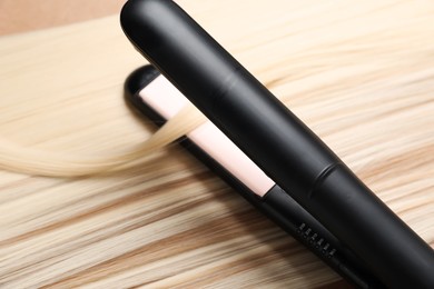 Photo of Modern flat iron on shiny blonde hair, closeup