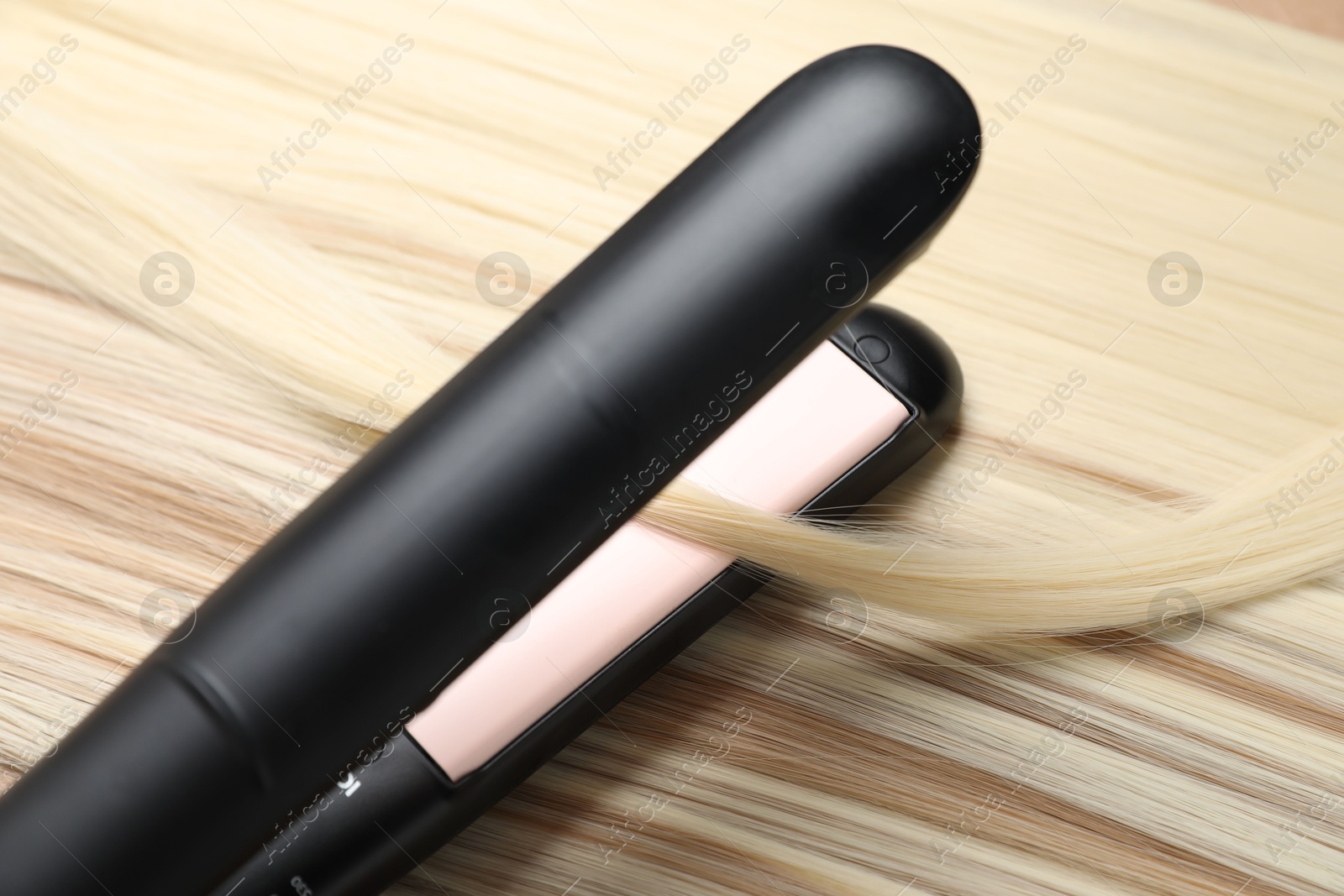 Modern flat iron on shiny blonde hair, closeup Photo of Modern flat iron on shiny blonde hair, closeup