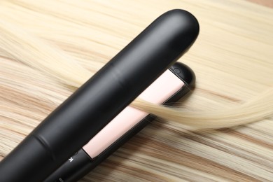 Photo of Modern flat iron on shiny blonde hair, closeup