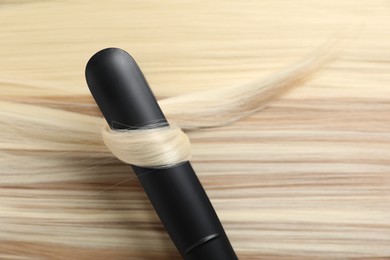 Photo of Modern flat iron on shiny blonde hair, closeup