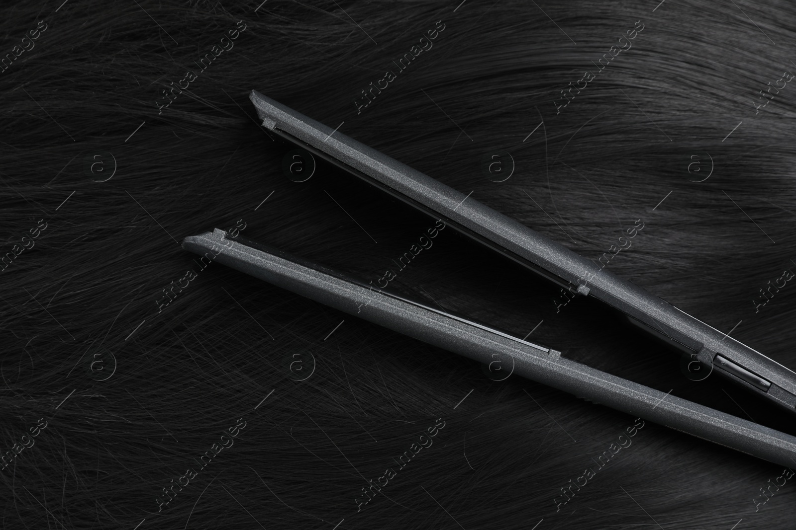 Photo of Modern flat iron on shiny black hair, top view