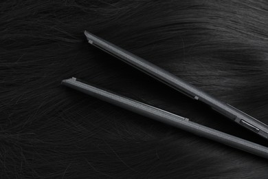 Photo of Modern flat iron on shiny black hair, top view