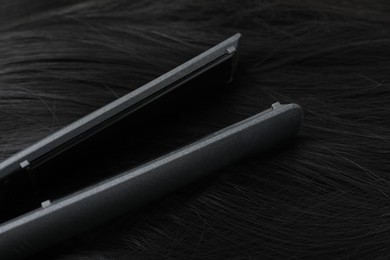 Photo of Modern flat iron on shiny black hair, closeup