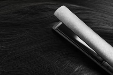 Photo of Modern flat iron on shiny black hair, closeup