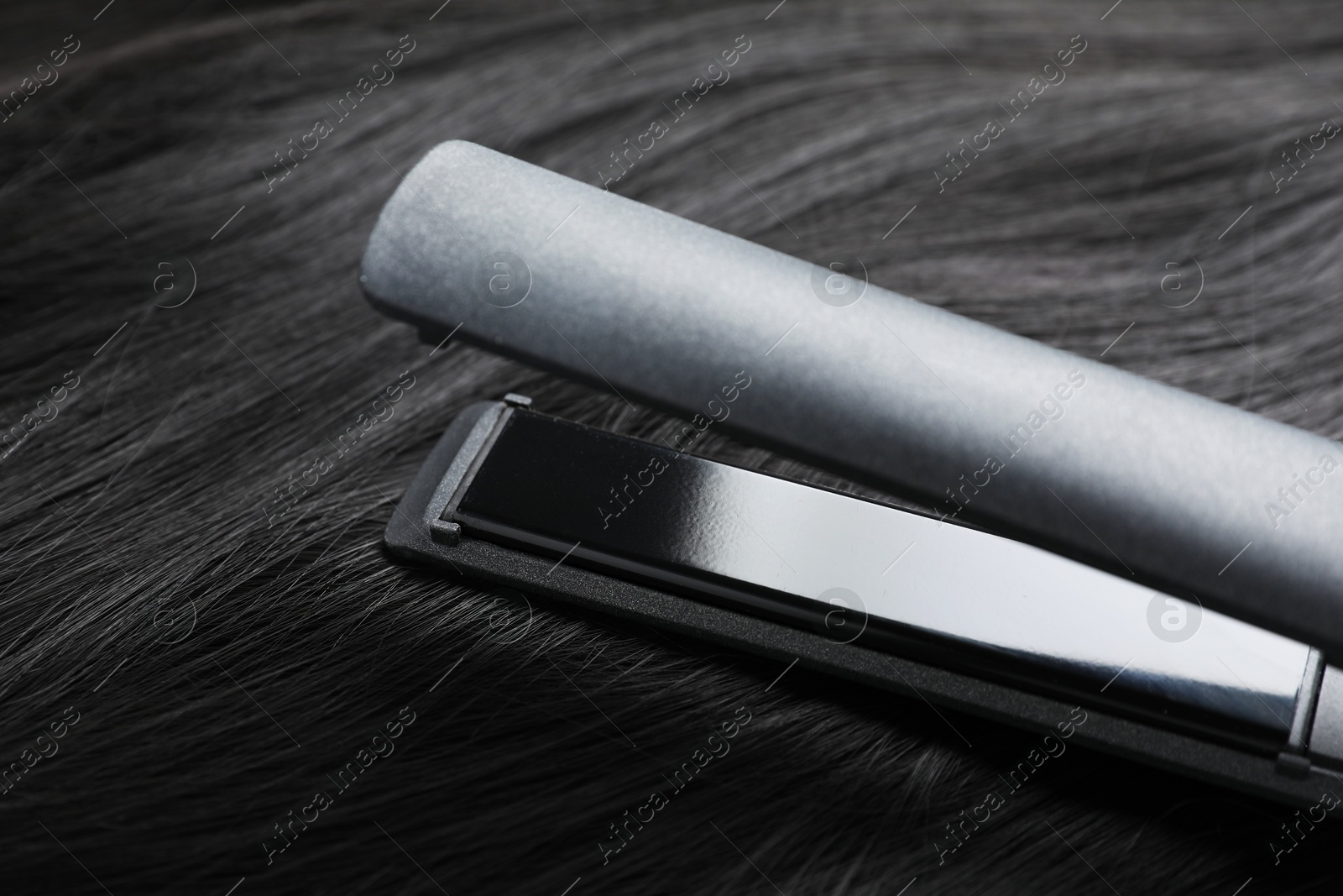 Photo of Modern flat iron on shiny black hair, closeup