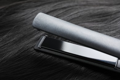 Photo of Modern flat iron on shiny black hair, closeup