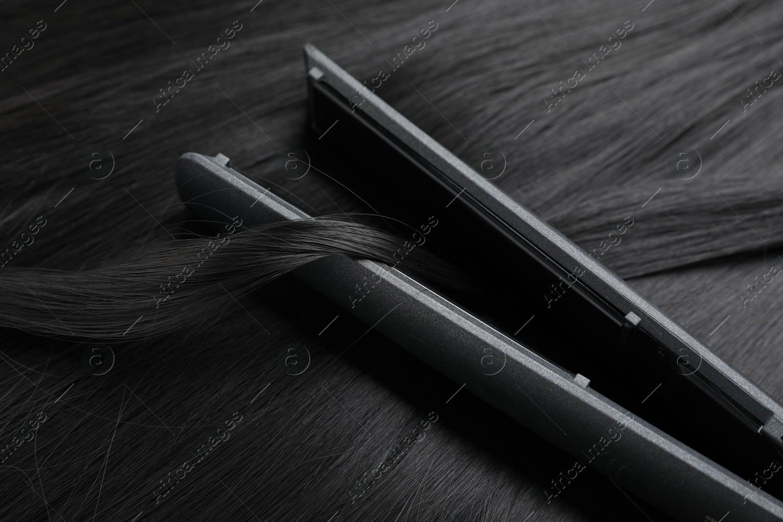 Photo of Modern flat iron on shiny black hair, closeup