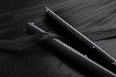 Photo of Modern flat iron on shiny black hair, closeup
