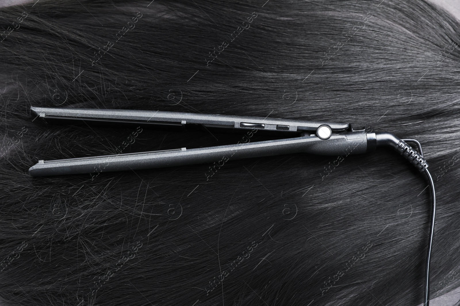 Modern flat iron on shiny black hair, top view Photo of Modern flat iron on shiny black hair, top view