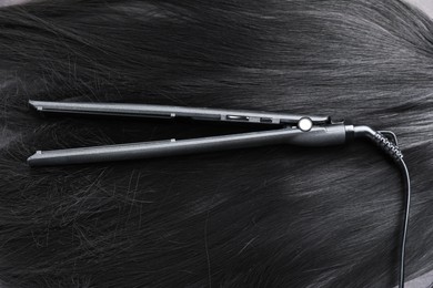 Photo of Modern flat iron on shiny black hair, top view