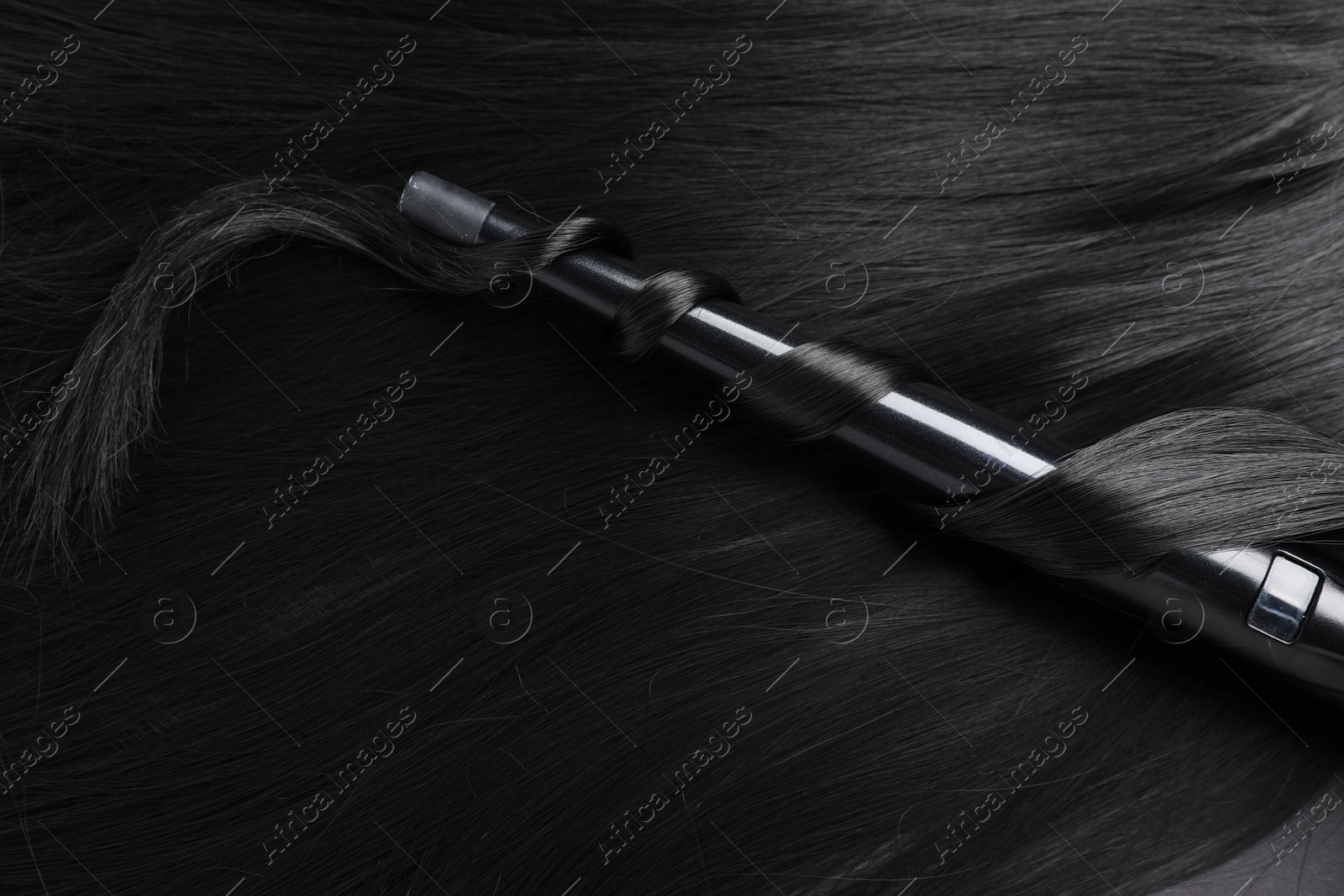 Photo of Curling iron with shiny black hair, closeup