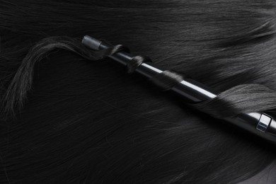 Photo of Curling iron with shiny black hair, closeup