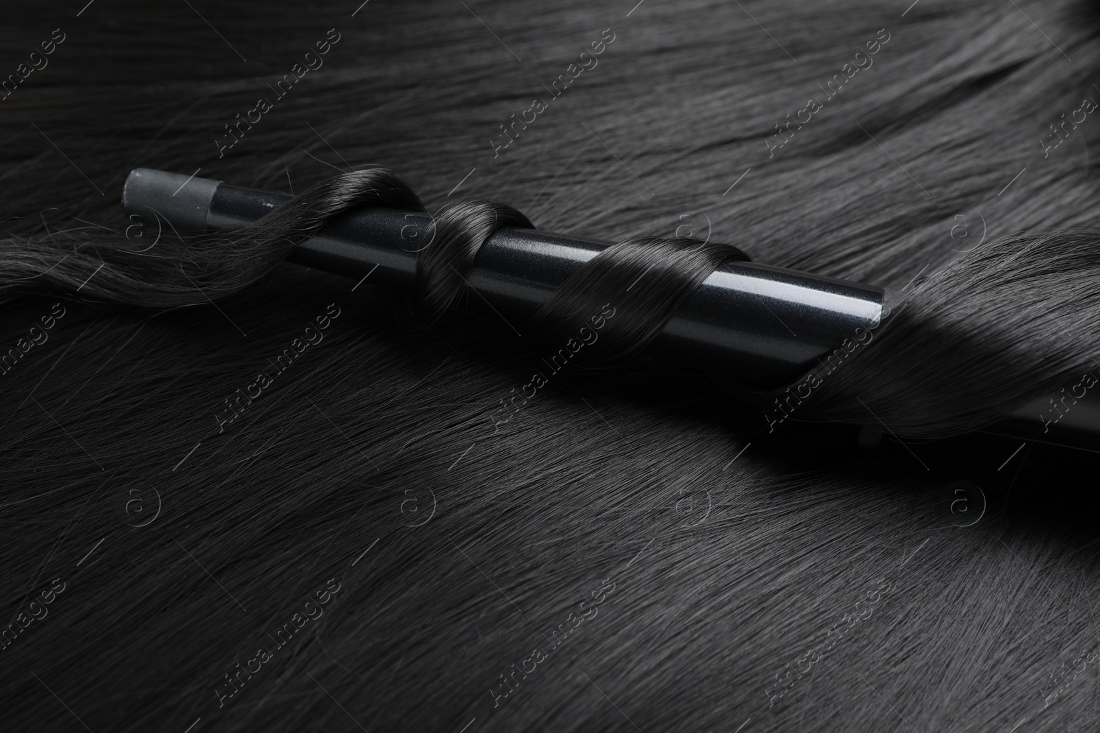Curling iron with shiny black hair, closeup Photo of Curling iron with shiny black hair, closeup