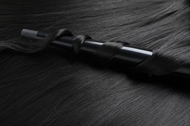 Photo of Curling iron with shiny black hair, closeup