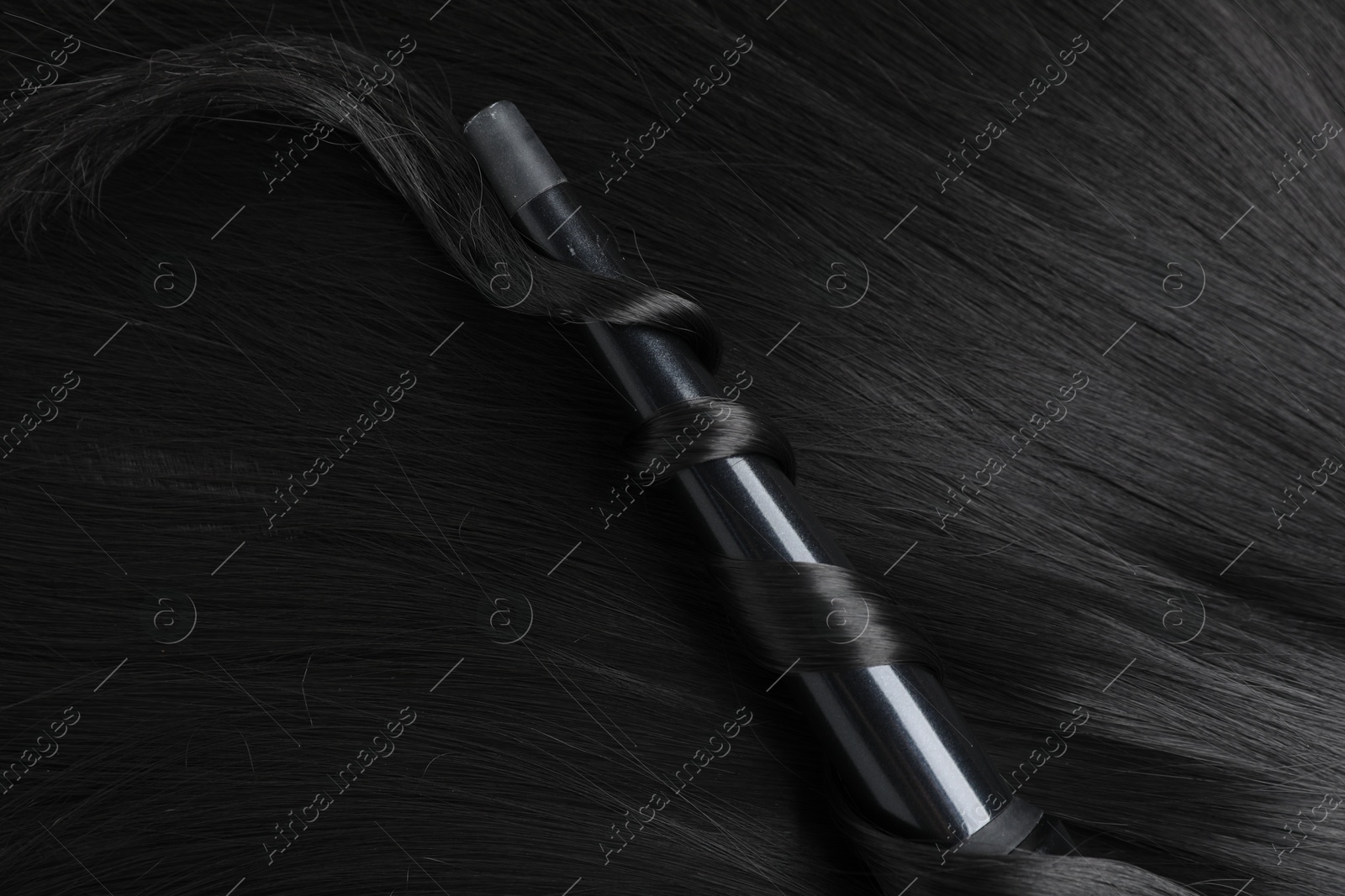 Photo of Curling iron with shiny black hair, top view