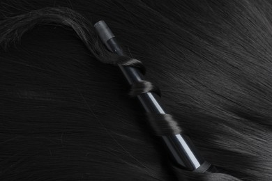 Photo of Curling iron with shiny black hair, top view