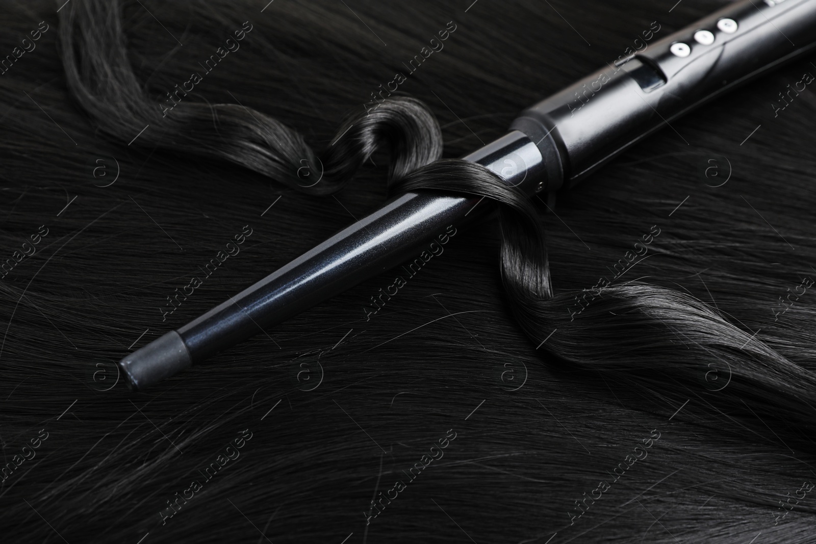Curling iron with shiny black hair, closeup Photo of Curling iron with shiny black hair, closeup