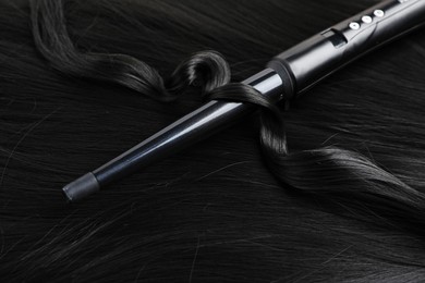 Photo of Curling iron with shiny black hair, closeup