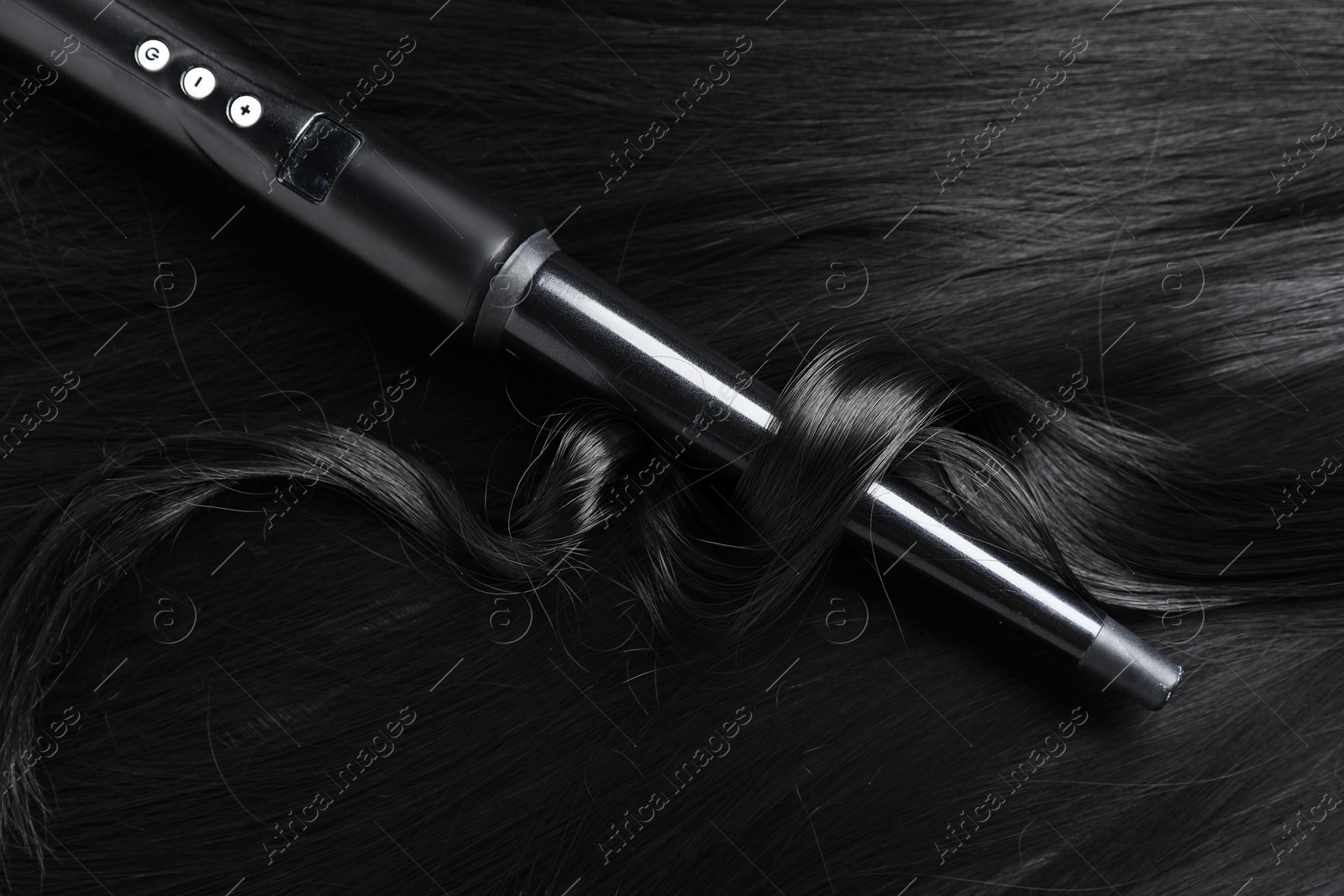 Curling iron with shiny black hair, closeup Photo of Curling iron with shiny black hair, closeup