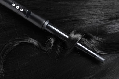 Photo of Curling iron with shiny black hair, closeup