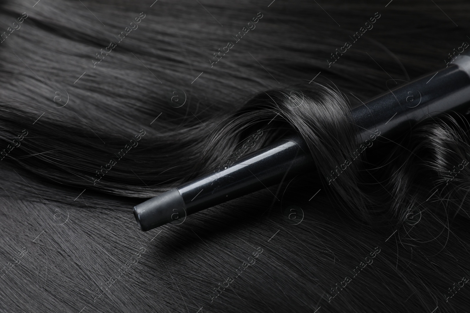 Curling iron with shiny black hair, closeup Photo of Curling iron with shiny black hair, closeup