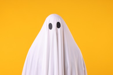 Photo of Creepy ghost. Man covered with white sheet on orange background